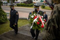 Dwóch Strażników Miejskich podchodzi do pomnika przy ul. Warszawskiej. Jeden z nich trzyma wiązankę kwiatów.