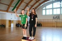 Nagrodzeni uczestnicy zawodów: chłopiec i dziewczynka z medalami na szyi trzymają w ręce statuetki biegacza.