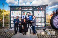 Trzech młodych kolarzy na podium. Poniżej przedstawiciele organizatorów LOTTO Poland Bike Marathon.