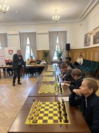 Kilku chłopców siedzących przy stołach z szachami na szachownicach.