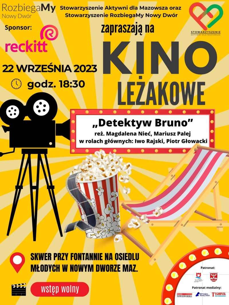 Czarna kamera na statywie, popcorn i klisza filmowa w kubku, w biało-czerwone pasy, drewniany leżak w biało-czerwone pasy.