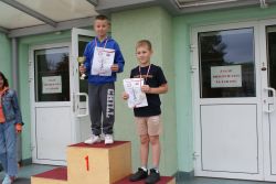 Dwóch chłopców stoi na podium. Jeden z pucharem i dyplomem, drugi z medalem i dyplomem.