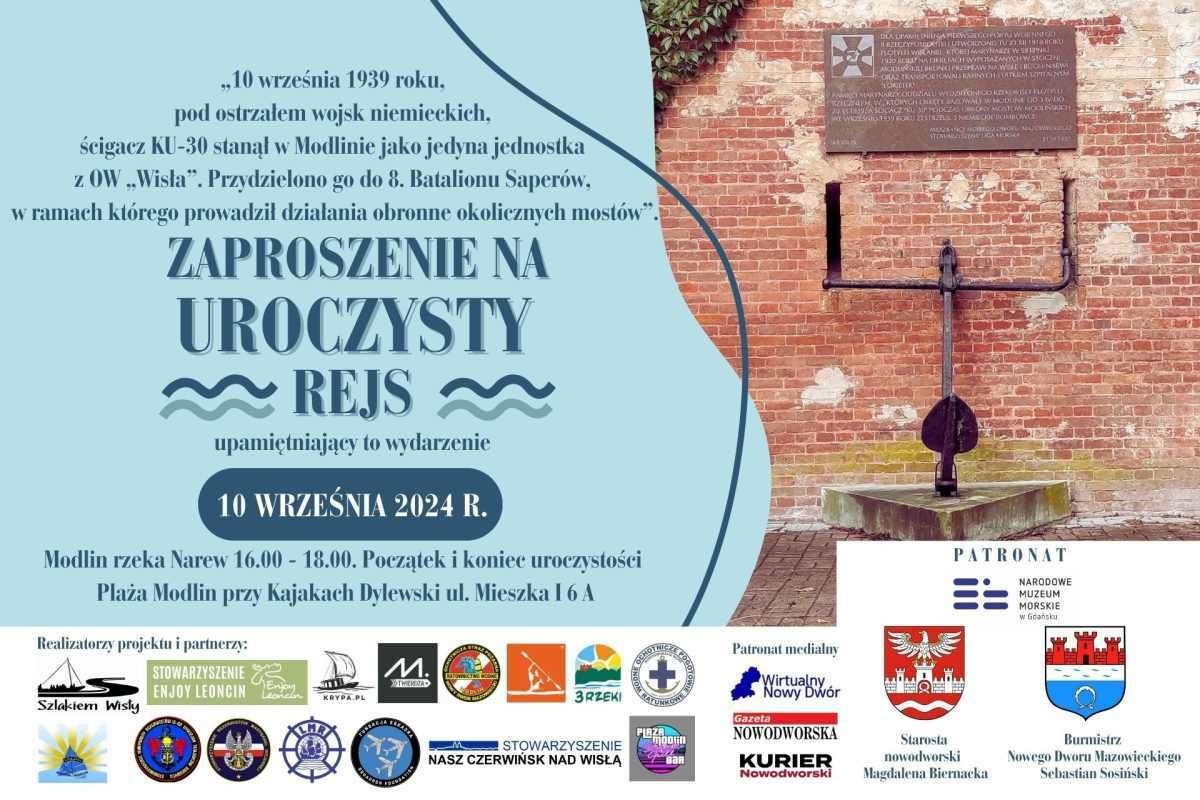 Kotwica okrętu pod pamiątkowa tablicą, oparta o mur z czerwonej cegły.