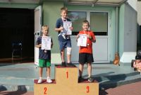Trzech chłopców z medalami i szyjach i dyplomami w rękach stoją na podium.