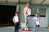 Trzy dziewczynki z medalami i szyjach i dyplomami w rękach stoją na podium.