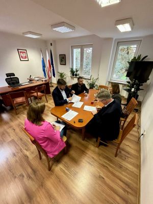 Przy stole siedzi trzech mężczyzn i dwie kobiety. Dwóch mężczyzn podpisuje dokumenty.