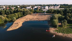 Kilkadziesiąt osób na plaży przy rzece. Poniżej pomarańczowy ponton z silnikiem i biały skuter wodny.