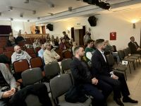 Kilkadziesiąt osób siedzi na krzesłach i patrzy w lewą stronę.