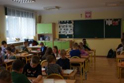 Dzieci siedzące na żółtych krzesełkach grają w warcaby.