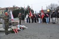 Dwóch mężczyzn w mundurach wojskowych przy pomniku z popiersiem mężczyzny. Młodzież ze sztandarami szkół.