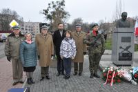 Dwie kobiety i pięciu mężczyzn: czterech w mundurach wojskowych, jeden w płaszczu przy pomniku z popiersiem mężczyzny.