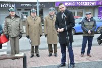 Mężczyzna w płaszczu mówi do mikrofonu na statywie.