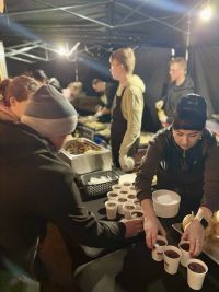 Mężczyzna bierze ze stołu kubek z płynem, a kobieta stawia dwa kubki z płynem.