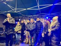 Za mężczyzną mówiącym do mikrofonu na scenie stoją cztery kobiety i czterech mężczyzn.