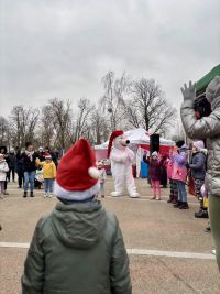 Osoba w stroju niedźwiedzia, w długiej czapce, kobieta i kilkoro dzieci stoją kółeczku z uniesionymi rękami.