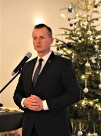 Mężczyzna w garniturze z krawatem mówi do mikrofonu.