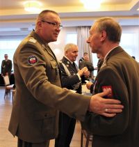 Dwóch mężczyzn w mundurach wojskowych jeden z nich dotyka prawą dłonią lewe ramię drugiego.