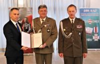 Mężczyzna w garniturze i mężczyzna w mundurze wojskowym trzymają wspólnie otwarte okładki z pismem w środku.
