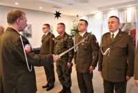 Mężczyzna w mundurze wojskowym dotyka lewego ramienia mężczyzny w mundurze wojskowym stojącym naprzeciwko niego.