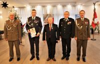 Mężczyzna w środku w garniturze po jego lewej i prawej stronie po dwóch mężczyzn w mundurach wojskowych.