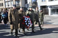 Czterech mężczyzn w mundurach wojskowych. Jeden z nich trzyma wiązankę kwiatów.