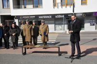 Mężczyzna w okularach i płaszczu mówi do mikrofonu na statywie.