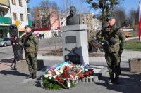 Dwóch mężczyzn w mundurach wojskowych z karabinami na piersiach stoją przy pomniku Marszałka Józefa Piłsudskiego.