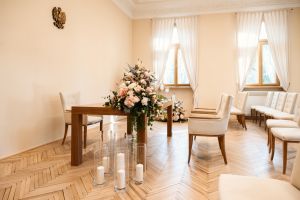 Kilka tapicerowanych jasnych krzeseł na drewnianych, brązowych nogach oraz brązowy, drewniany stół..
