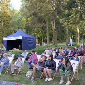 Kilkadziesiąt kobiet i mężczyzn siedzących na leżakach i patrzących do góry.