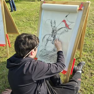 Chłopiec ryzujący rycerza na koniu, na papierze umieszonym na sztaludze.
