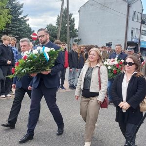 Dwóch mężczyzn i dwie kobiety idący razem obok siebie. Jeden z nich trzyma w rękach wiązankę kwiatów.