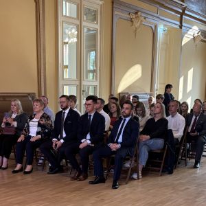 Kobiety i mężczyźni siedzący na krzesłach w dużej sali.