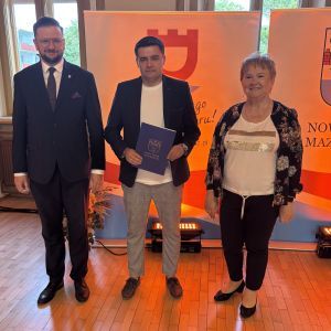 Mężczyzna z teczką trzymaną w dłoniach stoi pomiędzy mężczyzną i kobietą.