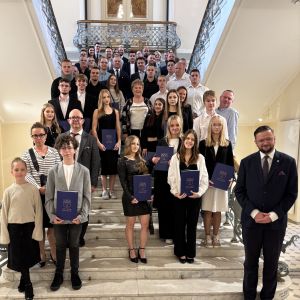 Grupa kilkudziesięciu dziewcząt, chłopców, kobiet i mężczyzn stoi na schodach patrząc przed siebie.