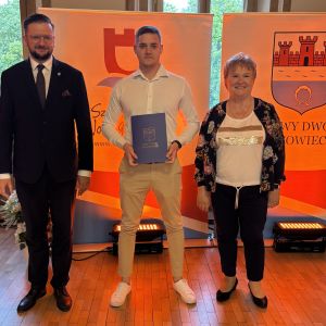 Mężczyzna z teczką trzymaną w dłoniach stoi pomiędzy mężczyzną i kobietą.