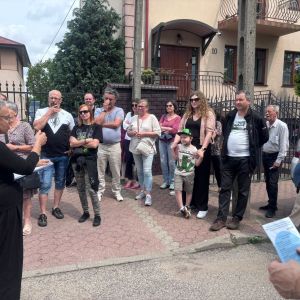 Grupa kobiet i mężczyzn stojących na chodniku patrzących w stronę kobiety stojącej przed nimi.