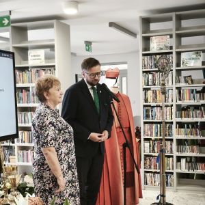 Kobieta i mężczyzna stojący obok szaty liturgicznej na stojaku.