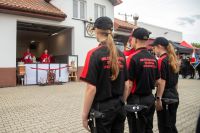 Dwie dziewczynki i chłopiec z toporkami strażackimi na pasach przed polowym ołtarzem z dwoma księżmi w czerwonych ornatach.