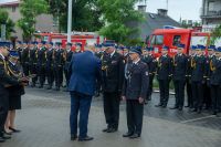 Dwóch mężczyzn w mundurach strażackich stojących przed mężczyzną w niebieskim garniturze.