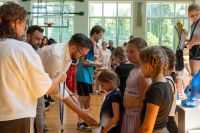 Mężczyzna w okularach wyciąga prawą dłoń do dziewczynki z medalem na szyi.
