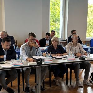 Kobieta i siedmiu mężczyzn siedzących przy stołach.