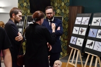 Kobieta i dwóch mężczyzn stojących obok dwóch sztalug ze zdjęciami samolotów wojskowych.