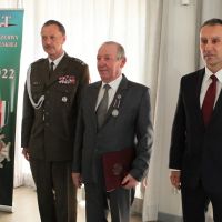 Mężczyzna w mundurze wojskowym i dwóch mężczyzn w garniturach stojących obok siebie.