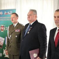 Mężczyzna w mundurze wojskowym i dwóch mężczyzn w garniturach stojących obok siebie.