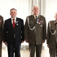 Mężczyzna w garniturze i trzech mężczyzn w mundurach wojskowych stojących obok siebie.