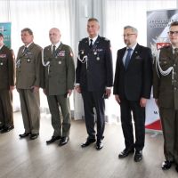 Mężczyzna w garniturze i pięciu mężczyzn w mundurach wojskowych stojących obok siebie.