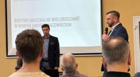 ekran z prezentacją, po prawej Burmistrz mówi do mikrofonu, na pierwszym planie osoby siedzące tyłem