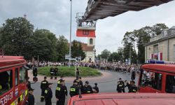 rondo, wkoło zebrane osoby, wóz strażacki z wysięgnikiem na którym wisi flaga