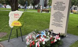 pomnik z wyrytym orłem, pod pomnikiem leżą kwiaty, w tle park