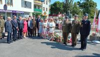 Kobiety, mężczyźni w garniturach i mundurach wojskowych przy pomniku.